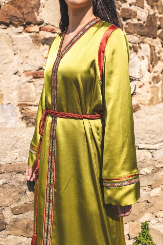 Détail de la bordure rouge et dorée du caftan FAIROUZ d'ANAE sur fond de ruines historiques.