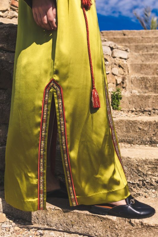 Détail de la bordure rouge et dorée du caftan FAIROUZ d'ANAE sur fond de ruines historiques.