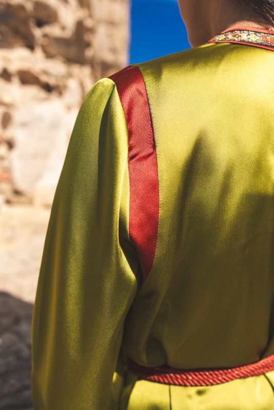 Détail de la bordure rouge et dorée du caftan FAIROUZ d'ANAE sur fond de ruines historiques.