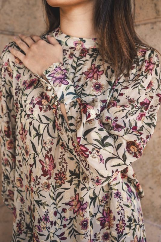 Blouse Wallin d'ANAE à manches longues avec imprimé floral, portée avec une jupe prune.