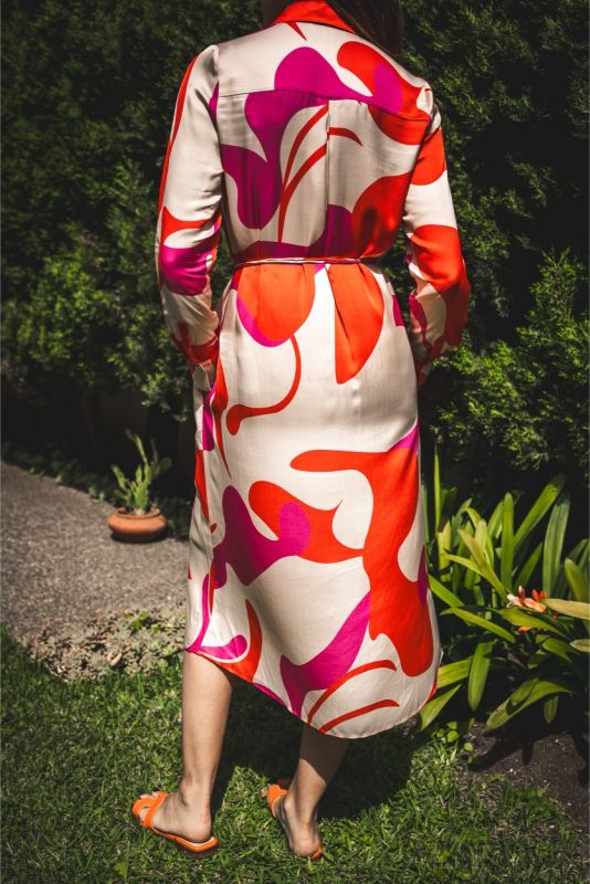Vue arrière de la robe 'Amalia' avec imprimé abstrait rouge et rose, ceinturée, évoquant élégance et dynamisme en extérieur.