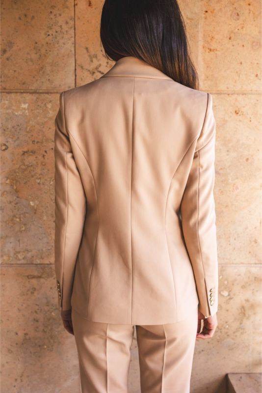 Vue arrière de la veste 'Frida' d'ANAE beige, mettant en évidence la coupe ajustée et les détails des manches pour un look chic.