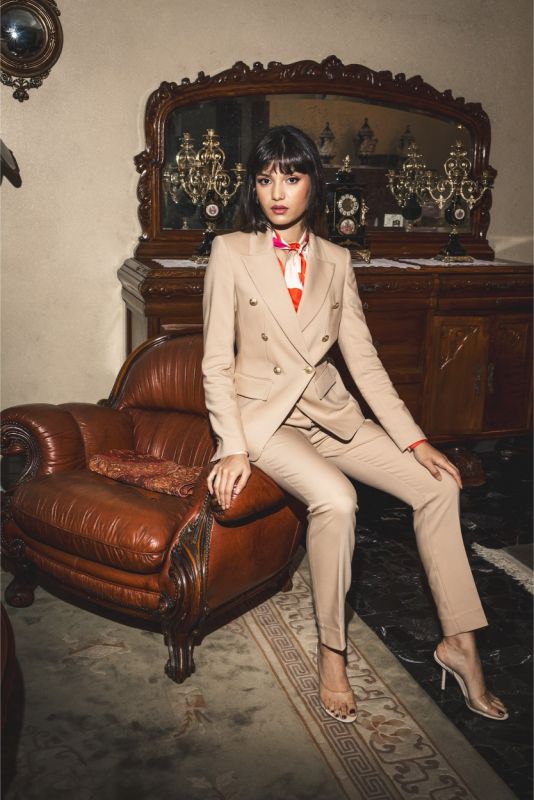 Détail de la veste 'Frida' d'ANAE avec boutons dorés, col cranté et poches à rabat, portée sur une blouse rouge et rose.