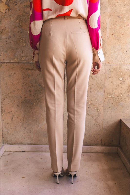Vue de dos du pantalon 'Frida' d'ANAE, en beige, montrant la coupe et les poches arrière, assorti à une blouse à motifs colorés.