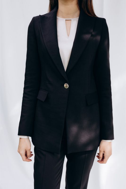 Femme chic en veste noire 'Lorena' d'ANAE, alliance de confort et d'élégance naturelle, prête pour toute occasion.