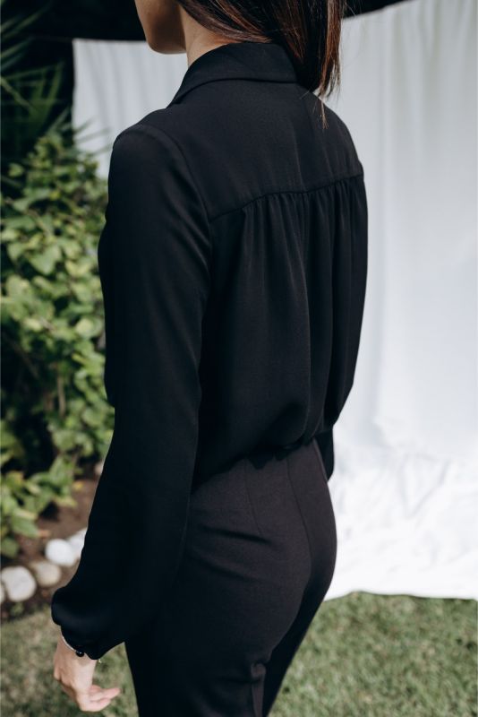 Dos de la blouse noire 'Belkis' d'ANAE, plis délicats, pour une allure féminine et professionnelle, vue en extérieur.