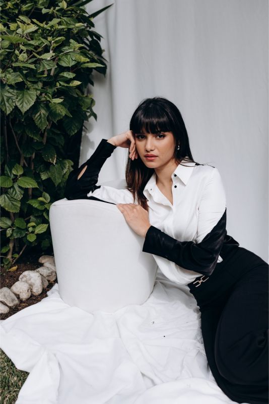 Femme tendance en chemise 'Celia' blanche à manches noires, posant avec assurance pour ANAE, mélange d'audace et de classe.