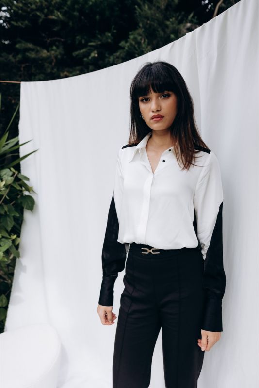 Femme tendance en chemise 'Celia' blanche à manches noires, posant avec assurance pour ANAE, mélange d'audace et de classe.