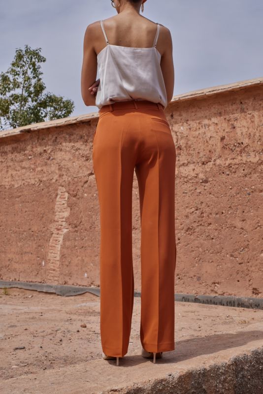 Vue arrière du PANTALON ROSARIO en whisky, montrant la coupe impeccable et le tissu de qualité sur un fond en terre cuite.