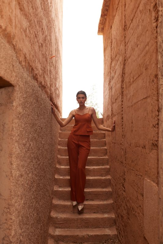 Femme élégante en top sans manches et PANTALON ROSARIO whisky, posant dans un escalier étroit pour une allure chic et moderne.