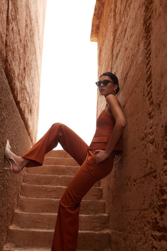 Femme élégante en top sans manches et PANTALON ROSARIO whisky, posant dans un escalier étroit pour une allure chic et moderne.