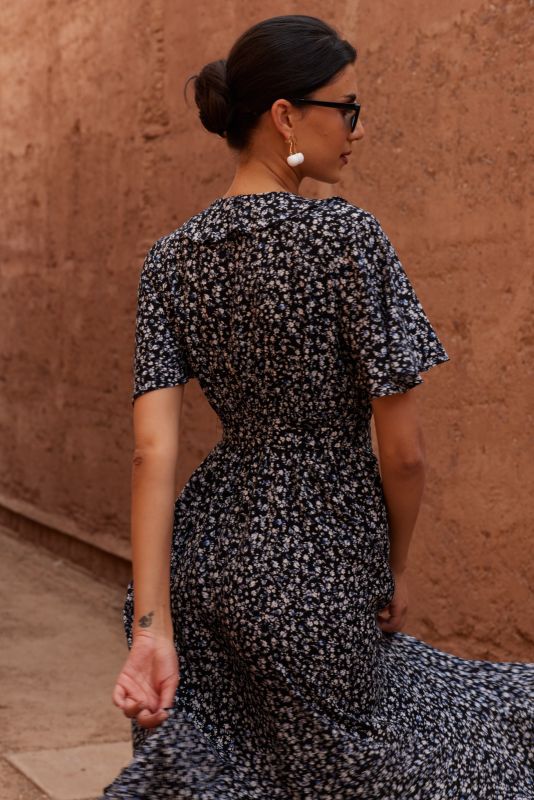Gros plan d'une robe noire à petites fleurs blanches et bleues, avec un détail de nœud à la taille.