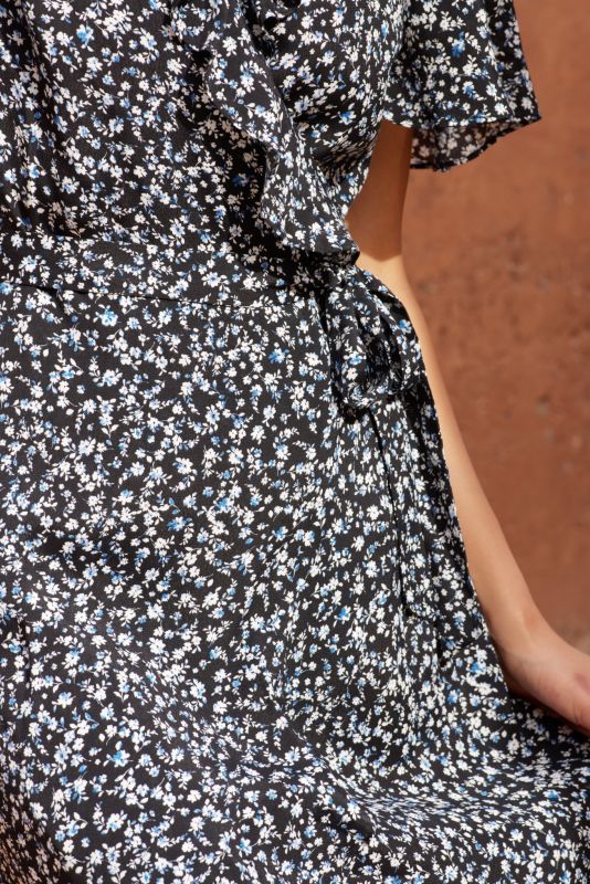 Gros plan d'une robe noire à petites fleurs blanches et bleues, avec un détail de nœud à la taille.