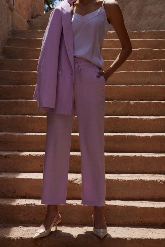 Femme portant le pantalon Teresa lilas avec une veste assortie drapée sur l'épaule.
