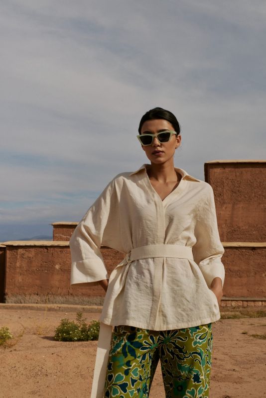 Vue latérale de la blouse Amanda beige avec une ceinture, portée par une femme avec des lunettes de soleil, en extérieur.
