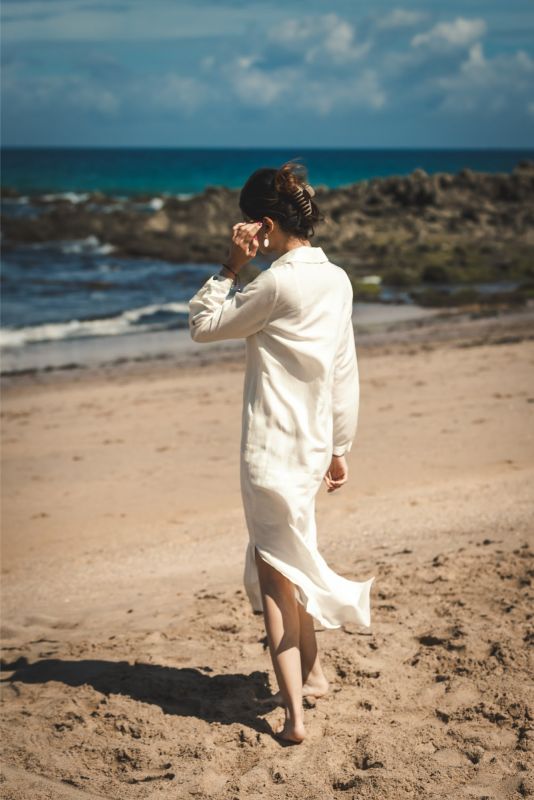 Femme marchant sur le sable, vue de dos, portant la robe Marta en lin blanc.