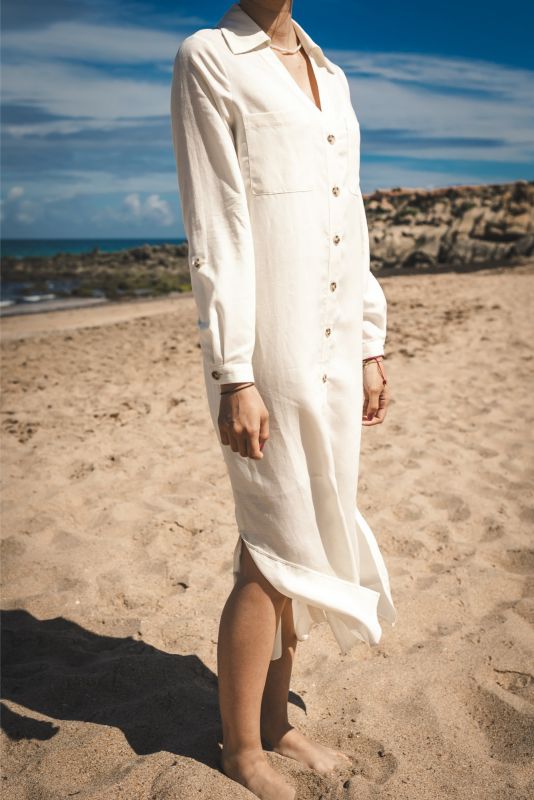 Femme marchant sur le sable, vue de dos, portant la robe Marta en lin blanc.